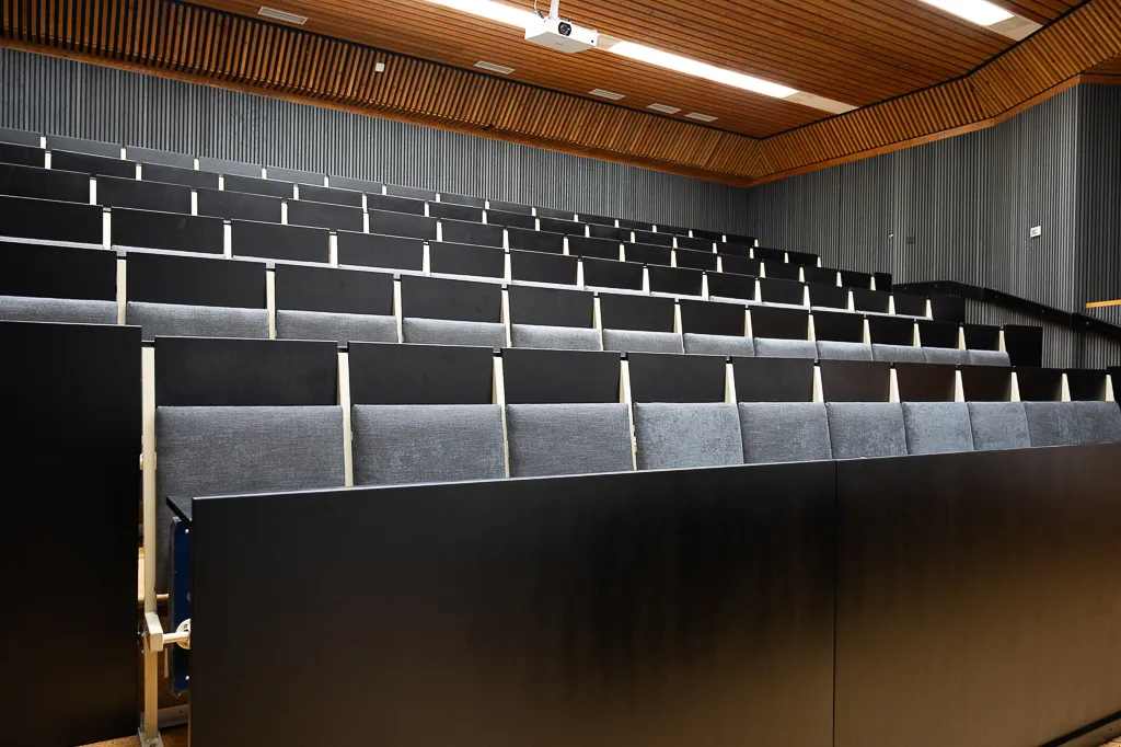 Tyhjä auditorio, mustat penkkirivistöt ja puinen katto.